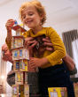 A child placing the Rhino figure at the very top of the tower, built by the HABA Rhino Hero Card Stacking Game