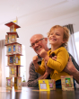 A child and adult happily playing the HABA Rhino Hero Card Stacking Game, sowing a fully build tower card stack