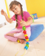 A child happily threading the Haba Wooden Bambini Beads onto the yellow cord whilst sat comfy on a blue cushion in a play room