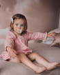 Young girl sat on a bed with a Hevea plastic-free baby pacifier in her mouth