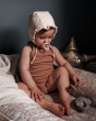 Young child sat on a cushion playing with some Hevea natural rubber toys, with a dummy in their mouth