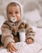 Close up of baby holding a bottle of milk with a Hevea natural rubber dummy in their mouth