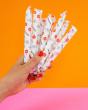 A person holding a bunch of Hey Girls Cardboard Applicator Tampons - Regular Absorbency, on an orange and pink background