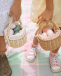 Two children holding the Olli Ella Rattan Berry Basket with Lining – Pansy Floral and Gumdrop in their hands. Inside each basket are colourful pink, blue and white eggs