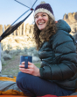An adult wearing a woolen purple and cream hat,  dark blue coat and trousers, is holding their Klean Kanteen Camping Mug in Dark Denim