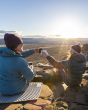 Two adults sat on top of a mountain, enjoying a hot drink in their Klean Kanteen 12oz Insulated Camping Mug, in the sunshine