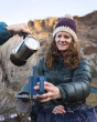 Adults enjoying a trip outdoors and having a hot drink in their Klean Kanteen Camping Mug. An adult is pouring a drink into the Dark Denim mug, which is being held by another adult relaxing on  a camping chair.