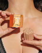 A person holding the Lamazuna Organic Sublime Orange Blossom Body Shimmer Solid Bar and box in their hands