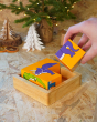 Close up of a hand holding a block from the Lanka Kade kids dinosaur puzzle above the other pieces, with a Christmas tree in the background