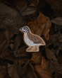 Lanka Kade Wooden Quail Toy, with light brown, white and black painted feather detail, nestled in a leafy background