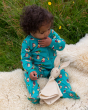 A child sat on a fluffy blanket and sucking their thumb is wearing the Little Green Radicals Garden Birds Organic Cotton Zip Babygrow, made from GOTS Organic Cotton, this cosy a teal footed babygrow has fun garden birds design, a full length zip and pocke