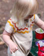 A child happily playing with a tea set whilst wearing the Little Green Radicals Oatmeal Fairisle Rainbow Knitted Shortie. The photo shows to pattern and button details on the front neck and chest