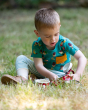 A child playing in a grassy field wearing the Little Green Radicals Garden Birds Organic T-Shirt & Jogger Playset, made from GOTS Organic Cotton, this cosy jogger set come with light blue and light cream striped jogger pants, a teal t-shirt with fun garde