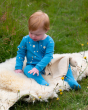A child gently stroking the fluffy blanket they're sitting on, wearing the Little Green Radicals Dawn Organic Cotton Zip Babygrow. Made from GOTS Organic Cotton, this beautiful blue babygrow features moon and start patters, a full length zip and a pocket 