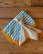 The Little Green Radicals Sail Away Organic Cotton Knitted Baby Blanket. Made from GOTS Organic Cotton, this soft blanket has light blue and cream wavy stripes with a yellow boarder. The Little Green Radicals Rabbit comforter toy is on top of the blanket