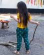 A child playing outside with a stick wearing Little Green Radicals Organic Cotton Little Lizard Comfy Joggers. Made with GOTS Organic Cotton, these joggers are a lovely deep forest green with a playful chameleon lizard print, a drawstring cord in the wais