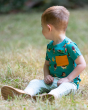 A child sitting in a grassy field, looking into the distance wearing the Little Green Radicals Garden Birds Organic T-Shirt & Jogger Playset, made from GOTS Organic Cotton, this cosy jogger set come with light blue and light cream striped jogger pants, a 
