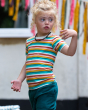 A child outside wearing the Little Green Radicals Rainbow Stripes Summer Short Sleeve T-Shirt. Made from GOTS Organic Cotton, this fun striped t-shirt comes with white, green, yellow, red and peach horizontal stripes, a white collar and popper fasteners o