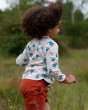 A child running and playing in a grassy field, wearing the Soft Red By The Sea Twill Shorts and a bird print top