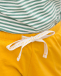 A closer view of the Gold Run Around Shorts. Made from GOTS Organic Cotton, these shorts are a rich gold colour, with off white piping on the legs, drawstring and side pockets for treasures