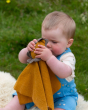 A child wearing blue dungarees playing with the Little Green Radicals Lion Organic Cotton Soft Toy on a grassy landscape background