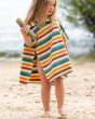 A child playing on the beach with a piece of drift wood, whilst wearing the Little Green Radicals Baby Rainbow Hooded Towel Poncho with the poppers open on the side