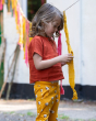 A child playing with coloured fabric on a line is wearing an orange top and Little Green Radicals Counting Sheep Organic Comfy Joggers.