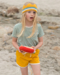 A child happily playing on a sandy beach wearing a green stripe top, crown and Gold Run Around Shorts. Made from GOTS Organic Cotton, these shorts are a rich gold colour, with off white piping on the legs, drawstring and side pockets for treasures