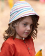 A side view of the stitching, material and rainbow stripe pattern on the Little Green Radicals Walnut Striped Reversible Sun Hat. A beautiful reversible sunhat made with GOTS Organic Cotton with rainbow stripes and a tie that fastens under the chin