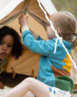 Two children playing in a cream tent. The child on the right is wearing the Little Green Radicals Organic Cotton From One To Another Sunshine Knitted Cardigan, and shows part of the sunshine design on the back