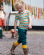Two children playing outside. The child in the front of the photo is wearing the Little Green Radicals Rainbow Stripes Summer Short Sleeve T-Shirt, green trousers and brown ankle boot wellingtons