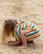 A child happily playing on a sandy beach whilst wearing the Little Green Radicals Baby Rainbow Hooded Towel Poncho.