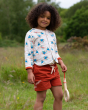 A child smiling and playing in a grassy field, wearing the Soft Red By The Sea Twill Shorts and a bird print top