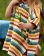 A closer look at the fabric, colours and sides of the Little Green Radicals Baby Rainbow Hooded Towel Poncho. In the photo, a child is also holding a small bunch of yellow flowers and blades of green grass