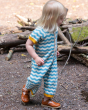 A side view of a child walking outside and wearing the Little Green Radicals Sail Away Knitted Shortie. Made from GOTS Organic Cotton, this shortie has a beautiful blue and cream wavy stripe with yellow arm and leg cuffs, with button on the chest and arou