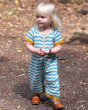 A child happily walking outside wearing the Little Green Radicals Sail Away Knitted Shortie. Made from GOTS Organic Cotton, this shortie has a beautiful blue and cream wavy stripe with yellow arm and leg cuffs, with button on the chest and around the crot