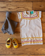 The Little Green Radicals Bear Organic Cotton Soft Toy displayed next to a cream LGR dress and yellow shoes, on a wooden floor background