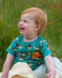 A toddler smiling happily wearing the Little Green Radicals Garden Birds Organic T-Shirt & Jogger Playset, made from GOTS Organic Cotton, this cosy jogger set come with light blue and light cream striped jogger pants, a teal t-shirt with fun garden birds 
