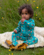 A child sat on a fluffy blanket and playing with soft plush toys, is wearing the Little Green Radicals Garden Birds Organic Cotton Zip Babygrow, made from GOTS Organic Cotton, this cosy a teal footed babygrow has fun garden birds design, a full length zip