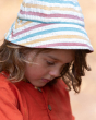 A child wearing the Little Green Radicals Walnut Striped Reversible Sun Hat. A beautiful reversible sunhat made with GOTS Organic Cotton with rainbow stripes and a tie that fastens under the chin