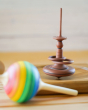 Mader childrens hand carved solid wood spinning top, spinning on a Mader spin plate next to a Mader rainbow lolly toy
