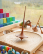 Mader wooden Trumpo spinning top on a Mader spinning plate surrounded by wooden spinning tops and a Grimms Large Stepped Pyramid