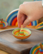 Close up of a hand holding a mader plastic free wooden sombrero spinning top on a mader spinning plate