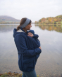 Woman stood by a lake carrying her baby in the Mamalila eco-friendly navy blue baby wearing all weather jacket