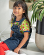 Young girl sat down wearing the Maxomorra eco-friendly navy denim pinafore dress over the short sleeve fox top