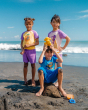 Three children stood together on a beach. The child on the left is wearing the Maxomorra Children's Organic Cotton Pineapple Raglan Short Sleeve Top and purple muslin shorts. The child in the middle is wearing the Maxomorra Monkey Raglan T-short and blue 