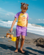 A child walking on the sand wearing the Maxomorra Children's Organic Cotton Pineapple Raglan Short Sleeve Top and purple muslin shorts