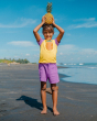 A child happily playing on the beach and holding a pineapple on top of their head, wearing the Maxomorra Children's Organic Cotton Pineapple Raglan Short Sleeve Top and purple shorts