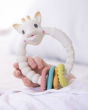 A closer look at the Sophie la Girafe® - So'Pure Multi-textured Sensory Teether Ring, showing the white Sophie Giraffe ring, with the multicoloured, textured ring at the bottom, being held in a child's hand