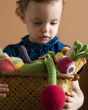 Girl holding a basket full of Myum handmade crochet soft vegetable toys in front of a beige wall 